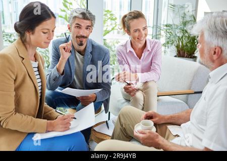 Lächelnde Geschäftskollegen, die sich in der Lounge über Dokumente austauschen Stockfoto