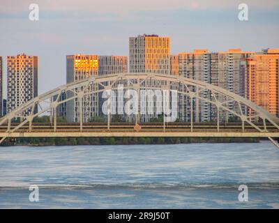 Arc Bridge über den Fluss mit modernem Stadtgebäude bei Sonnenuntergang mit Copy Space Foto Stockfoto