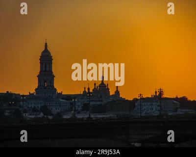 Die goldene Morgendämmerung in Kiew. Blick auf die Kiew-Pechersk Lavra und das linke Ufer. Silhouette Panorama bei Sonnenuntergang über dem bunten Himmel über dem Dnieper River mit Stockfoto