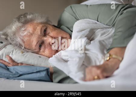 Nahaufnahme einer Seniorin, die auf ihrem Bett liegt und sich ausruht. Stockfoto