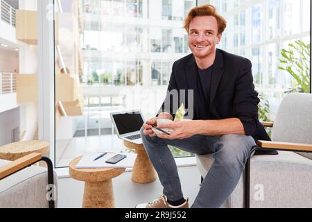 Ein lächelnder rothaariger Geschäftsmann träumt in der Bürolounge Stockfoto