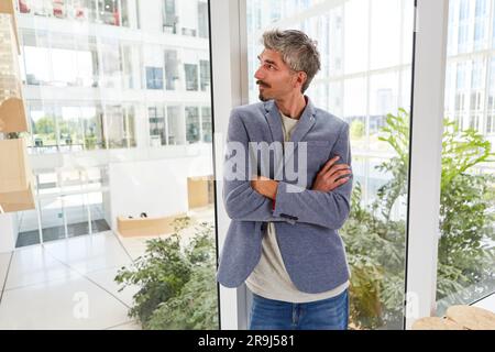 Ein Geschäftsmann, der die Arme am Fenster gekreuzt hat, während er am Tag träumte Stockfoto