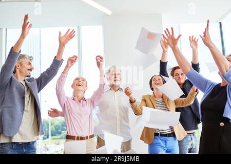 Glückliche Geschäftsleute jubeln und werfen im Büro Papierbögen zusammen Stockfoto