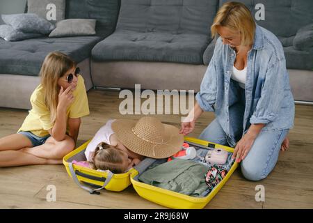 Mutter mit Töchtern, die einen gelben Koffer für die Reise packen. Die Familie hat Spaß beim Urlaub. Glückliches Kind, das sich im Koffer vorbereitete Stockfoto
