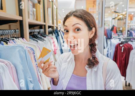 Eine Frau nimmt eine Bankkarte aus ihrer Brieftasche, während sie Kleidung in einem Einkaufszentrum einkauft Stockfoto