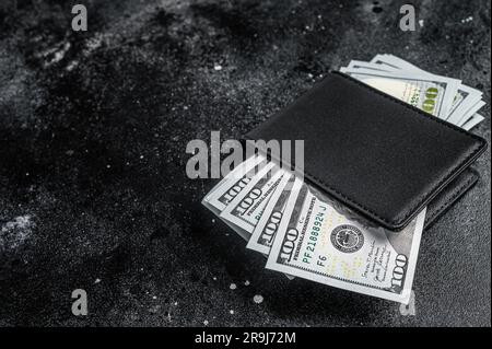 Eine schwarze Handtasche mit dem großen Päckchen Dollar, Bargeld-Schein. Schwarzer Hintergrund. Draufsicht. Speicherplatz kopieren. Stockfoto