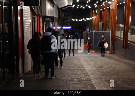 Blick auf die Rückseite einer Schlange oder Schlange von Personen außerhalb von United Currency Exchange in QV Melbourne bei Nacht Stockfoto