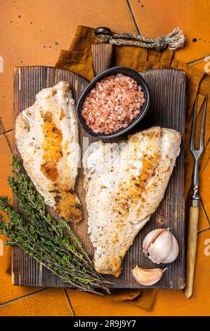 Rotes Meerbarschfilet, Rotbarsch auf Holzbrett. Orangefarbener Hintergrund. Draufsicht. Stockfoto