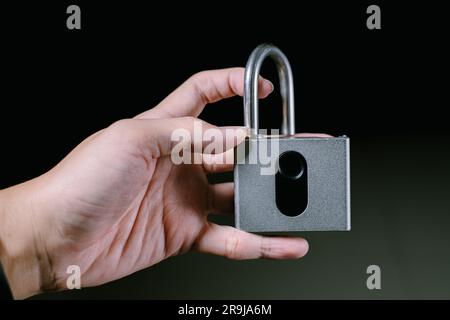 Eine Hand hält ein entriegeltes Vorhängeschloss mit Fingerabdruck. Isolierter schwarzer Hintergrund. Geeignet für Werbung. Stockfoto