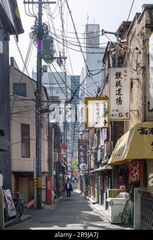 Kyoto, Japan – April 2023; vertikaler Blick auf eine der engen Straßen der Stadt mit traditionellen Gebäuden, Schildern und vielen Stromleitungen, die scheinbar hängen Stockfoto