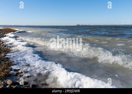 Blick aus dem niedrigen Winkel auf die Wellen von Eis, slurpee oder Slush am Kieselstrand Greenwich Point, Greenwich, CT, USA mit Eisbildung am Strand und Long Island in Stockfoto