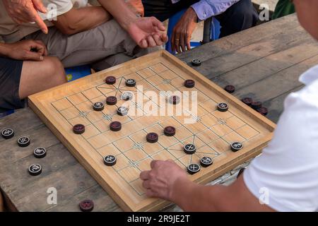 Blick aus einem hohen Winkel auf das Brett des Spiels Xiangqi, auch chinesisches Schach oder Elefantenschach genannt, mit Händen von Spielern und Beobachtern an Bord des Sunds Stockfoto