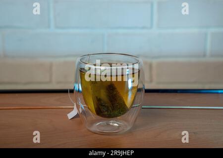 Teeglasbecher mit Teebeutel für Nahaufnahmen. Tee in einer durchsichtigen Tasse zubereiten. Stockfoto
