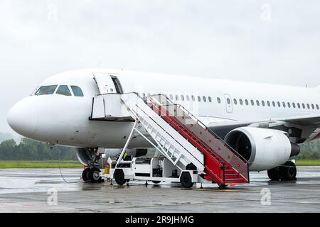 Große moderne Flugzeuge mit Leiter, die für den Flug am bewölkten Tag auf dem Flughafen vorbereitet sind Stockfoto