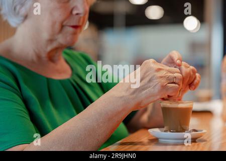 Geerntete, anonyme ältere Frau in grünem T-Shirt sitzt an der Holztheke und trinkt Kaffee in der Flughafen-Cafeteria Stockfoto