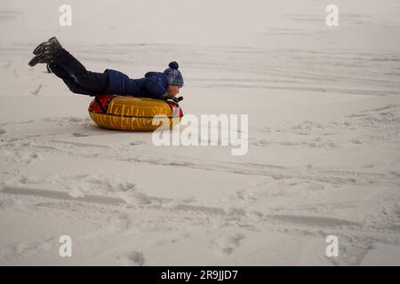 Der Junge rennt fröhlich auf dem Tubing durch die verschneite Ebene. Frohe Winterferien. Schneeaktivitäten. Stockfoto