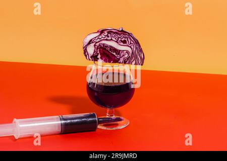 Zusammensetzung von Glas mit hausgemachtem Rotkohl-Saft mit Rotkohl und Spritzennaher vor orangefarbenem Hintergrund Stockfoto