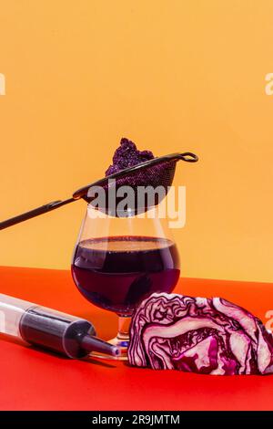 Zusammensetzung von Glas mit Sieb und Spritze gefüllt mit hausgemachtem Rotkohlsaft vor hellem Hintergrund Stockfoto