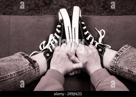 Die Beine des Mädchens sind mit klassischen Turnschuhen ausgestattet. Ein Turnschuh am Bein eines Mädchens. Teenager Füße in lässigen neuen Sneakers auf dem Sofa Nahaufnahme Bild. Vintage-Style Stockfoto