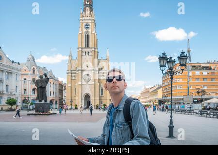 Ein Tourist mit einer Sightseeing-Karte, der draußen in der Altstadt steht. Porträt eines gutaussehenden männlichen Reisenden Rucksacktouristen mit Sonnenbrille mit Karte und Stockfoto