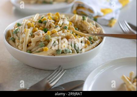 Nudelsalat mit Mayonnaise, Mais, grünen Erbsen, Schinken und gekochten Eiern in einer Schüssel Stockfoto