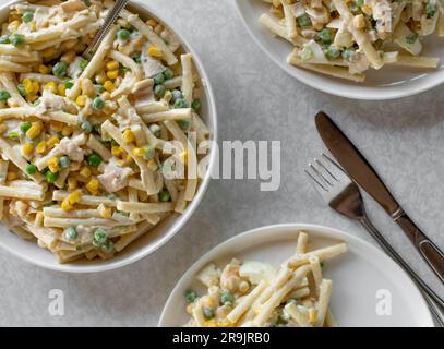 Klassischer Nudelsalat mit Mayonnaise, gekochten Eiern, Mais, grünen Erbsen, Zwiebeln und Wurst in einer Schüssel auf hellem Hintergrund von oben Stockfoto