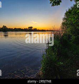 Das Foto zeigt einen faszinierenden Sonnenuntergang über dem Croxall Lake in Großbritannien. Der Himmel ist in leuchtenden Orange-, Pink- und Lila-Tönen gehalten Stockfoto