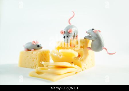 Kleine Plastikmäuse und ein Stück Käse mit Löchern. Weißer Hintergrund. Stockfoto