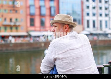 Ein Mann mit Strohhut, der auf der Flussbrücke steht und auf den Fluss schaut. Stockfoto