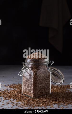 Leinsamen in einem Glasgefäß auf grauem, strukturiertem Hintergrund. Gesundes Essen, Superfood. Stockfoto