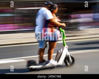 Leute, die in der King Street in Hammersmith, London, mit hoher Geschwindigkeit unterwegs sind, verschwommen von langer Belichtung, zeigen zwei Personen auf einem E-Scooter Stockfoto