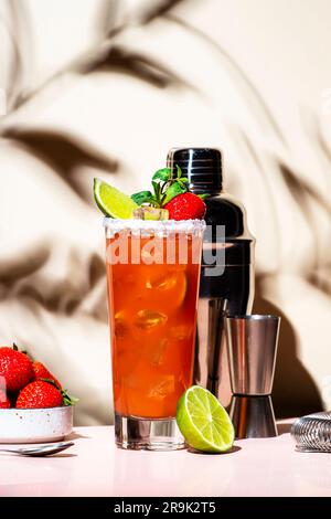 Paloma Cocktailgetränk mit Silbertequila, Grapefruit- und Limettensaft, frischen Erdbeeren, Minze und Eis im Glas mit Salzrand. Beigefarbener rosafarbener Hintergrund., Stockfoto