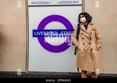 Eine Dame mit Gesichtsmaske steht neben einem Liverpool Street Elizabeth Line Schild an der Liverpool Street London U-Bahnstation Stockfoto