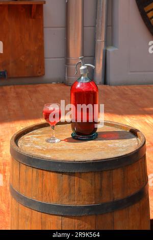 Auf dem Foto stehen ein alter Glasheber und ein Glas gefüllt mit einem Getränk aus roten Früchten auf einem Holzfass vor dem Eingang zum Café Lviv. Stockfoto