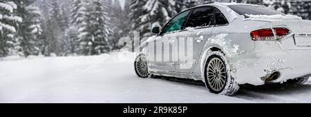 Silbernes Auto mit Eis bedeckt auf einer schneebedeckten Straße, Blick von hinten, verschwommener Baumhintergrund, leerer Platz für Text links Stockfoto