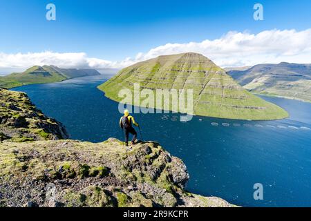 Wanderer mit Rucksack bewundern den Fjord und Kunoy Island auf Felsen auf dem Berg Klakkur, Klaksvik, Bordoy Island, Färöer Inseln Stockfoto