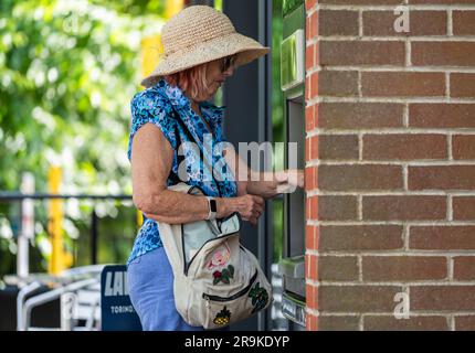 Seniorin, die Geld in bar, an einem Geldautomaten, einem Geldautomaten oder einem Geldautomaten in Großbritannien bekommt. Stockfoto