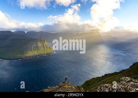 Blick aus der Vogelperspektive auf entfernte Wanderer auf Felsen mit Blick auf den Fjord im Sommer, Vidoy Island, Färöer Inseln Stockfoto