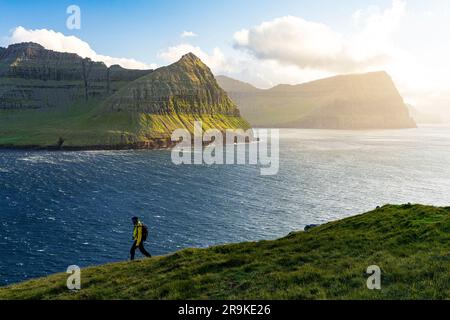 Wanderer genießen einen Spaziergang auf Klippen mit Blick auf den Fjord bei Sonnenuntergang, Vidoy Island, Färöer Inseln Stockfoto