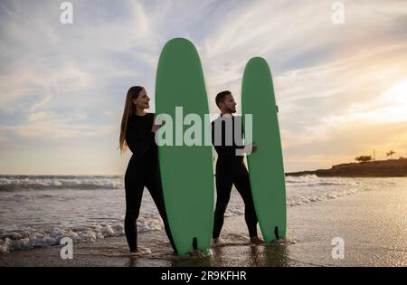 Fröhliches Junges Paar In Neoprenanzügen Surfen Am Strand Zusammen Stockfoto