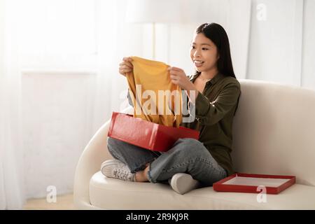 Glückliche junge koreanische Frau, die zu Hause das Paket auspackt Stockfoto