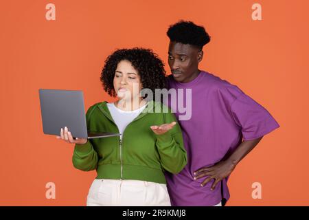 Unglückliches multikulturelles Paar, das auf den Bildschirm schaut und Gesten macht Stockfoto