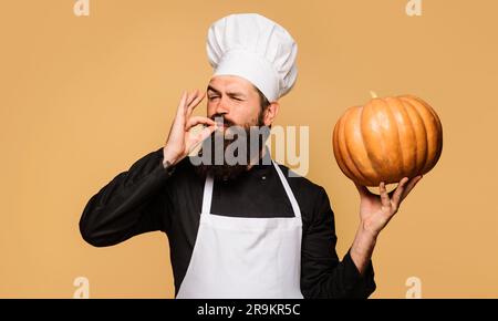 Männlicher Koch mit Kürbis, der das Schild in Ordnung zeigt. Bärtiger Mann in Koch-Uniform mit Kürbis. Bio-Lebensmittel. Gesundes Produkt. Erntefest. Thanksgiving Stockfoto