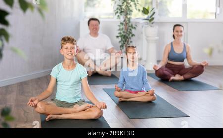 Teenager-Mädchen mit ihren Eltern praktiziert Yoga in Lotusposition Stockfoto