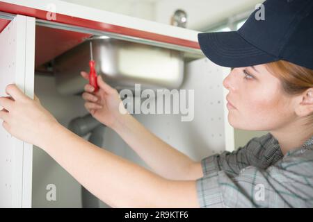 Eine junge Frau repariert die Rohre unter dem Spülbecken Stockfoto