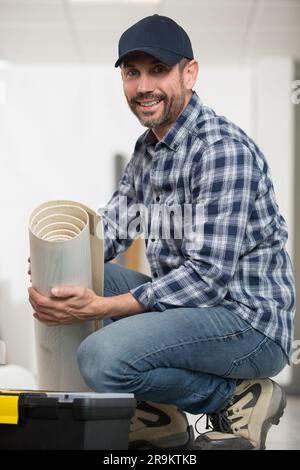 Männlicher Handwerker Rollteppich auf dem Boden zu Hause Stockfoto