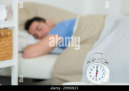 Wecker auf Tisch Mann schläft im Bett im Hintergrund Stockfoto