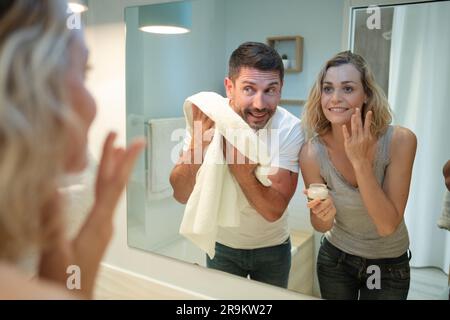 Ein Paar, das seine Waschgänge macht und in den Badezimmerspiegel schaut Stockfoto