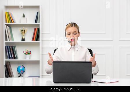 Der Kundenservice ist eine süße Frau in einem weißen Hemd mit Headset und Computer, die auf den Bildschirm zeigt Stockfoto