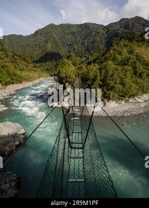 Die Hängebrücke aus Metall in der Caesspool Gorge führt über den türkisfarbenen, kristallklaren, blauen Wasserfluss am Arahura River an der Westküste der Südinsel Neuseeland Stockfoto